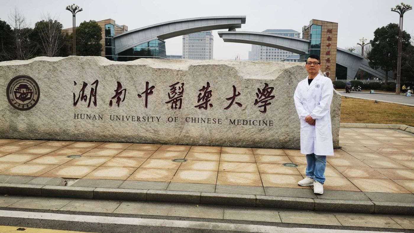 Peng i hvid kittel foran indgangsstenen til Hunan University of Chinese Medicine.